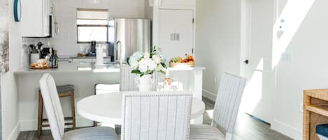 Una cocina moderna con electrodomésticos blancos, una isla central con asientos y una zona de comedor con sillas a rayas.