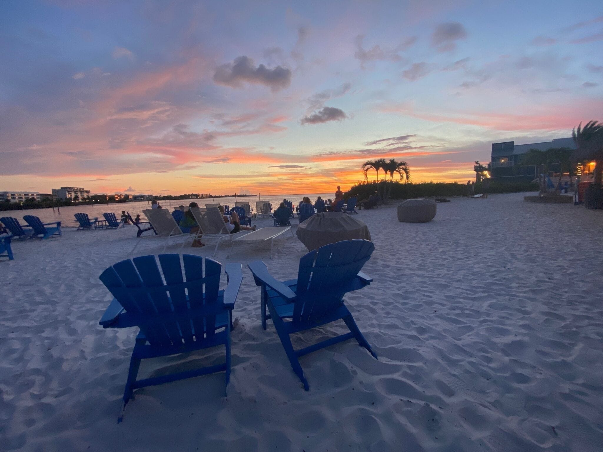 Una playa con filas de sillas azules y un paraguas grande, con vista al océano al atardecer.