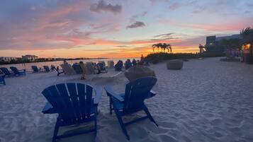 Una playa con filas de sillas azules y un paraguas grande, con vista al océano al atardecer.