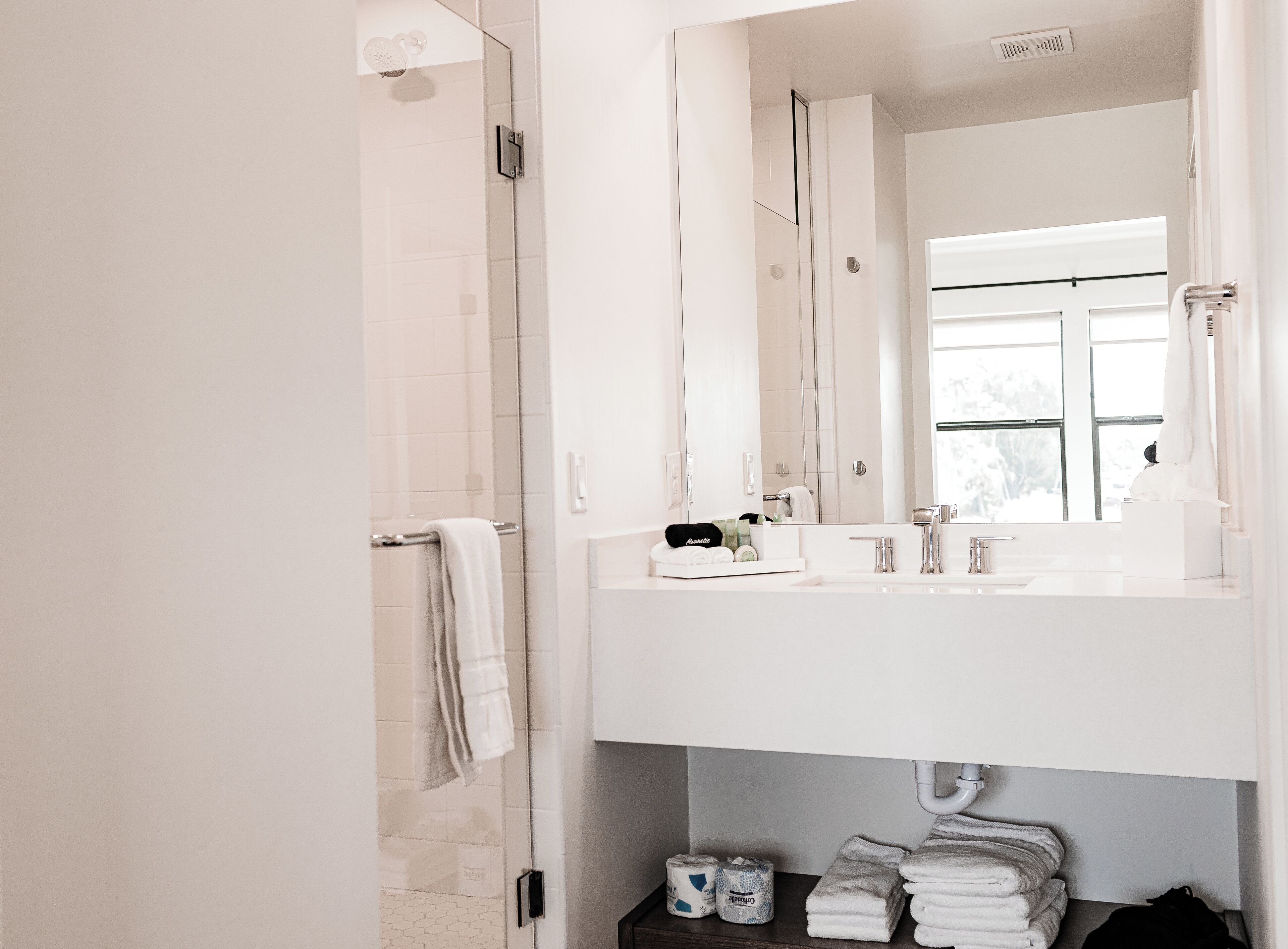 Une salle de bain moderne avec un grand miroir, des éléments d’aménagement blancs et une douche à parois de verre.
