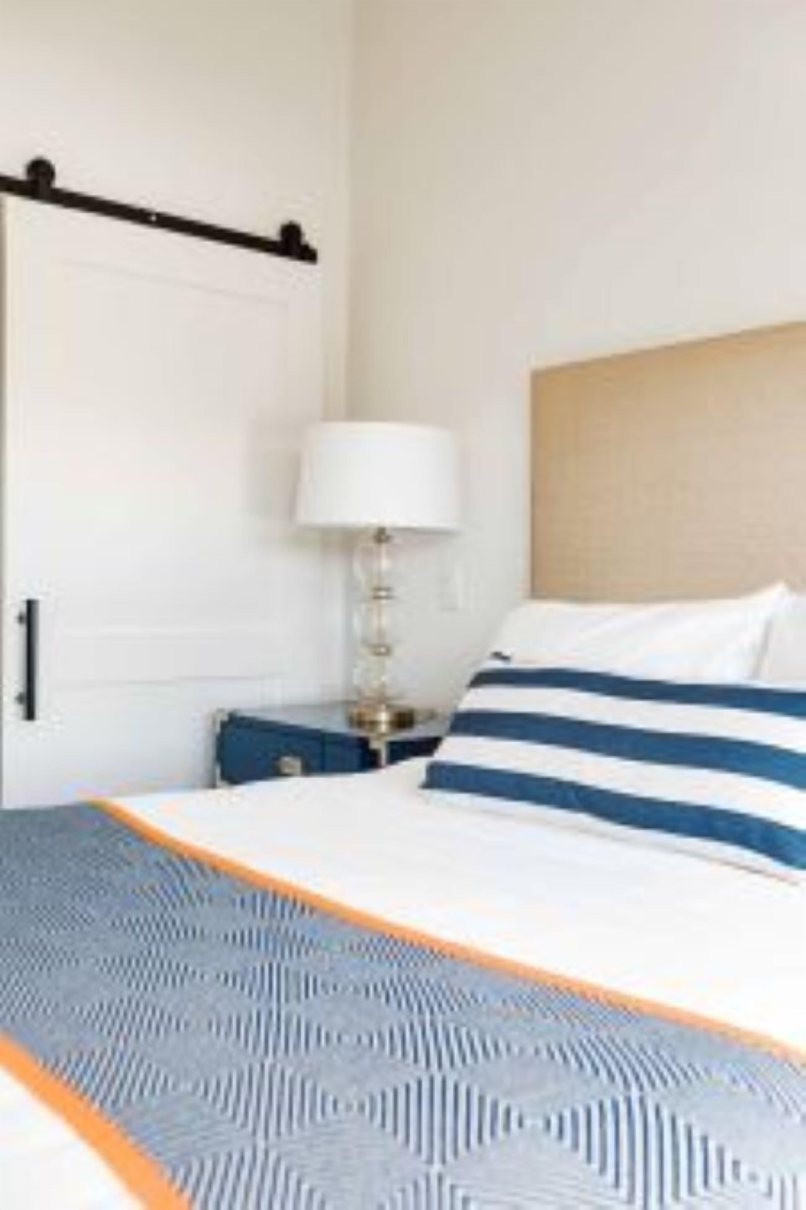 Una habitación de hotel con una cama, una mesita de noche, una lámpara y una puerta.