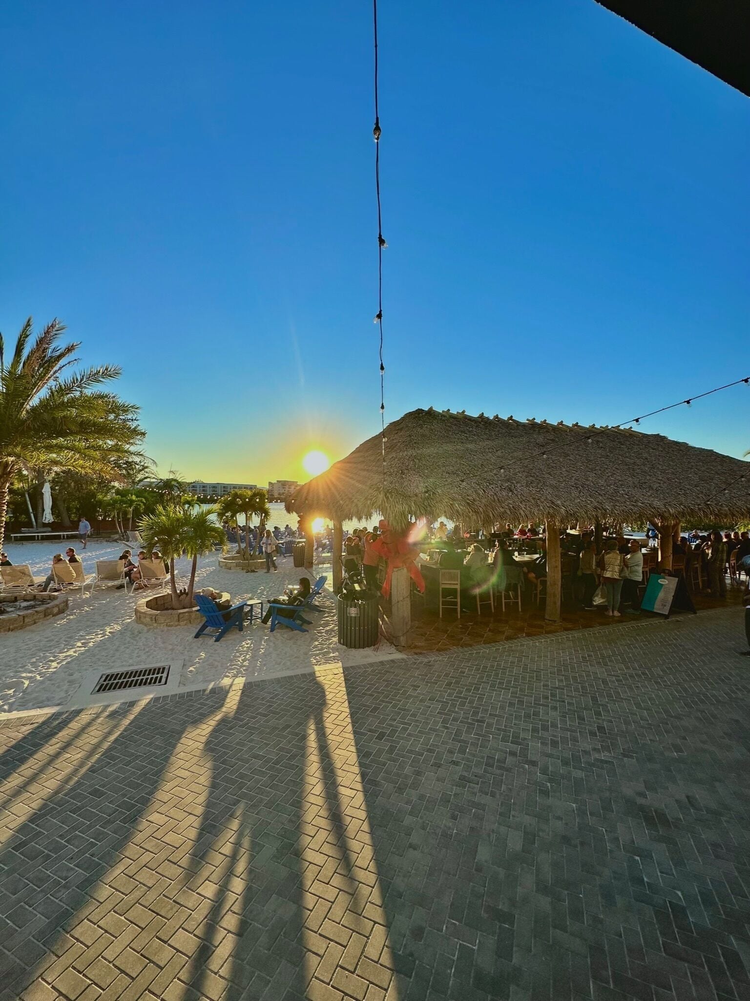 Un restaurante frente a la playa con terraza, techo de paja y vistas al océano.