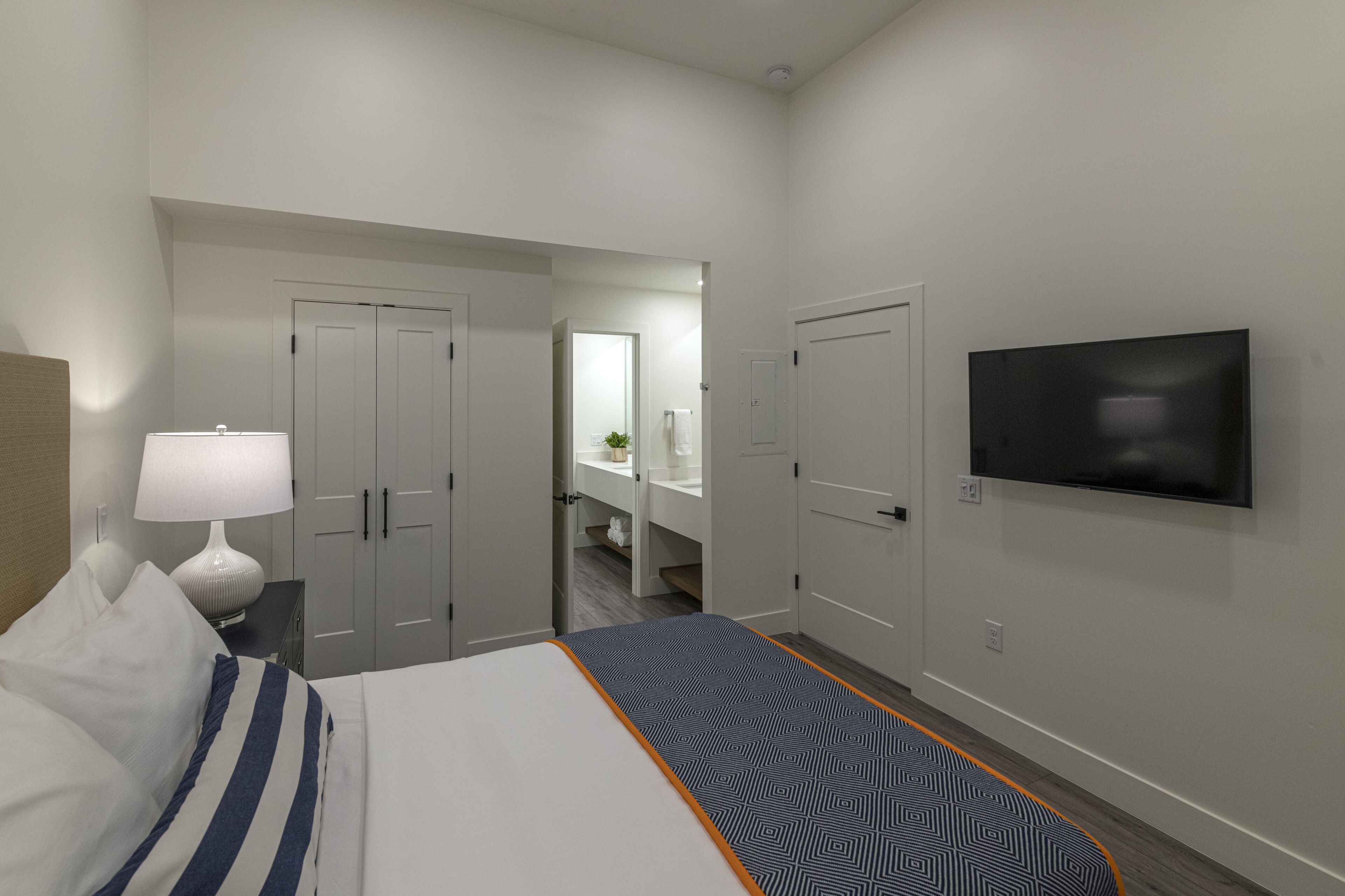 Habitación de hotel con cama, televisor, escritorio con lámpara y baño visible a través de una puerta abierta.