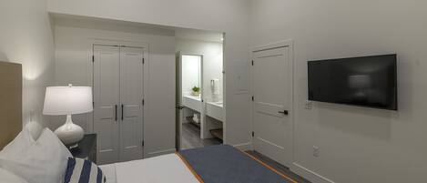 Habitación de hotel con cama, televisor, escritorio con lámpara y baño visible a través de una puerta abierta.