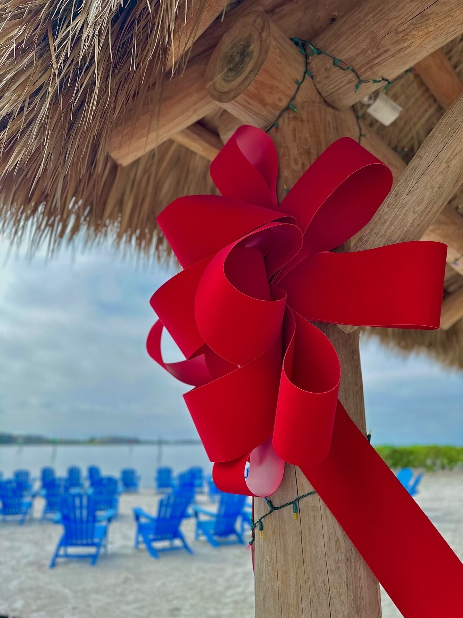 A wooden structure with a red ribbon tied in a bow, overlooking a beach with blue chairs.
