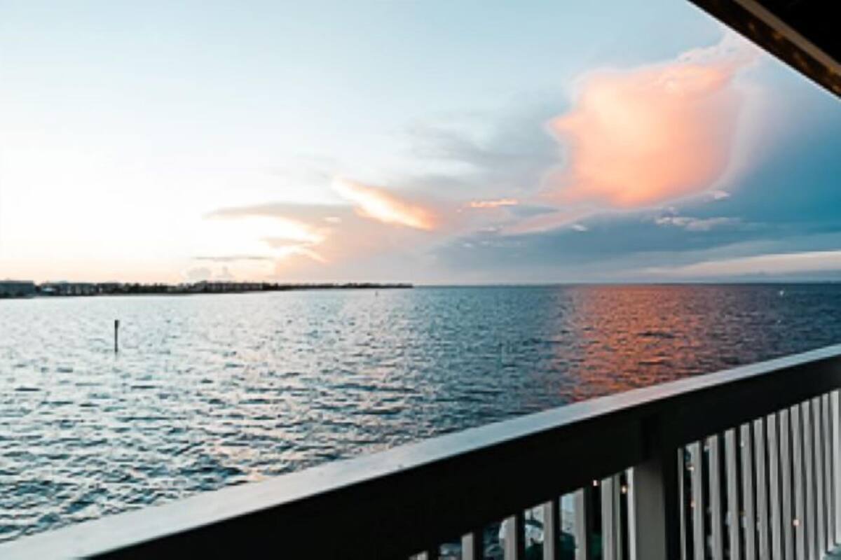 A view from a balcony overlooking a body of water with a distant shoreline and a sunset.