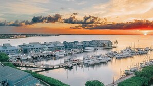 A marina with boats docked, a waterfront building complex, and a sunset in the background. - The Suites at Fishermen’s Village (Punta Gorda)