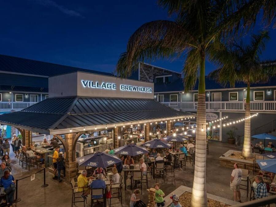 A Village Brewhouse with outdoor seating and palm trees.