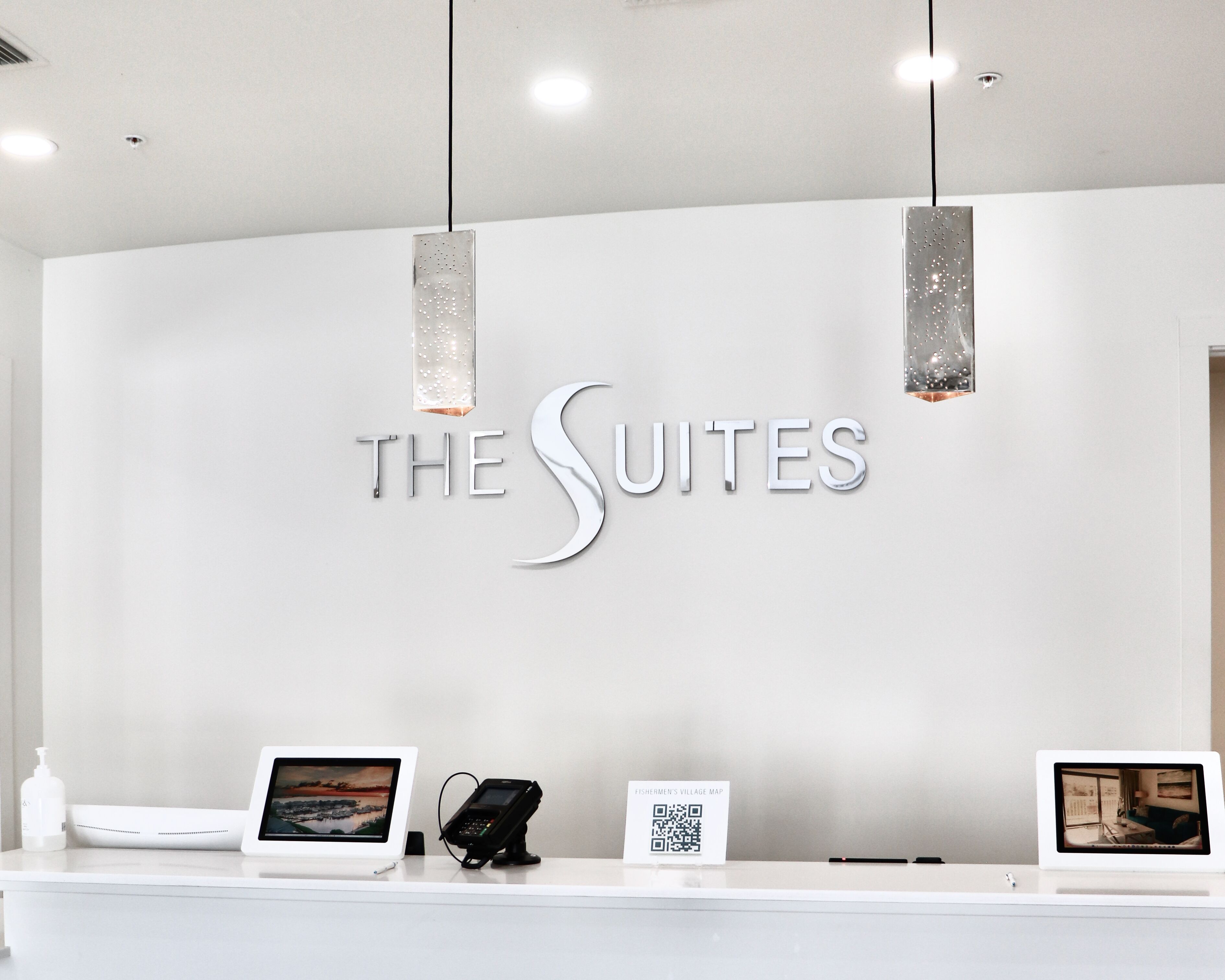 Una reception con una segnaletica che riporta "THE SUITES" e un codice QR per una mappa del villaggio.
