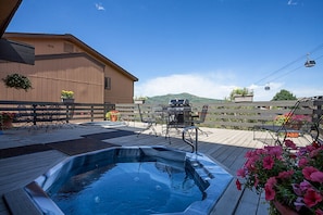 Relax in a serene hot tub on a deck surrounded by lush greenery and breathtaking mountain views.