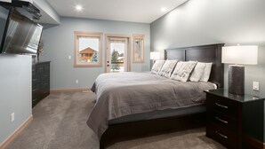 Un dormitorio con cama, cómoda, televisor y ventanas.