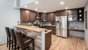 Una cocina moderna con una isla central, taburetes de bar, un refrigerador de acero inoxidable y un microondas.