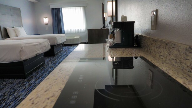 Une chambre d’hôtel avec deux lits, un téléviseur à écran plat, une machine à café et un coin cuisine moderne doté d’un plan de travail et d’un évier.
