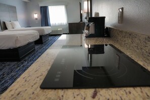 Une chambre d’hôtel avec deux lits, un téléviseur à écran plat, une machine à café et un coin cuisine moderne doté d’un plan de travail et d’un évier.