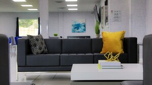 Un espace de bureau moderne avec un canapé noir, une table basse blanche et un coussin jaune.