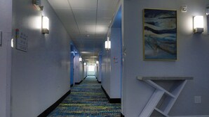 Un couloir d’hôtel avec un tapis à motifs, des appliques murales et un tableau.