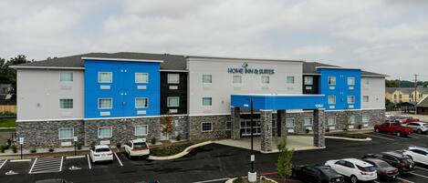 A multi-story hotel with a modern design, featuring a mix of white and blue exterior walls, and a parking lot with several cars.