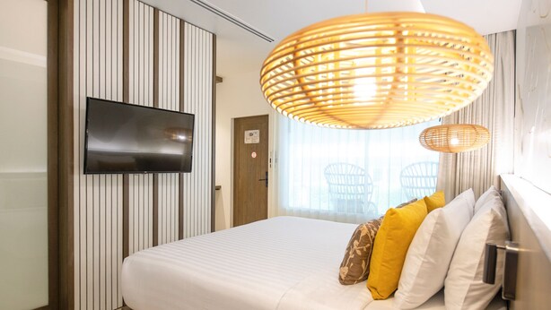 Habitación de hotel con cama, televisor montado en la pared, puerta y ventana con cortinas.