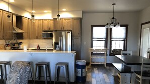 A modern kitchen with wooden cabinets, stainless steel appliances, and a bar area with stools.