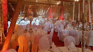Un salón de banquetes con mesas redondas dispuestas para un evento formal, con manteles blancos, cristalería y candelabros.