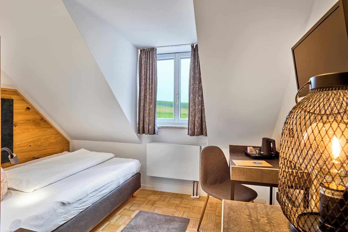 A bedroom with a bed, a desk, a chair, a lamp, and a window with curtains.