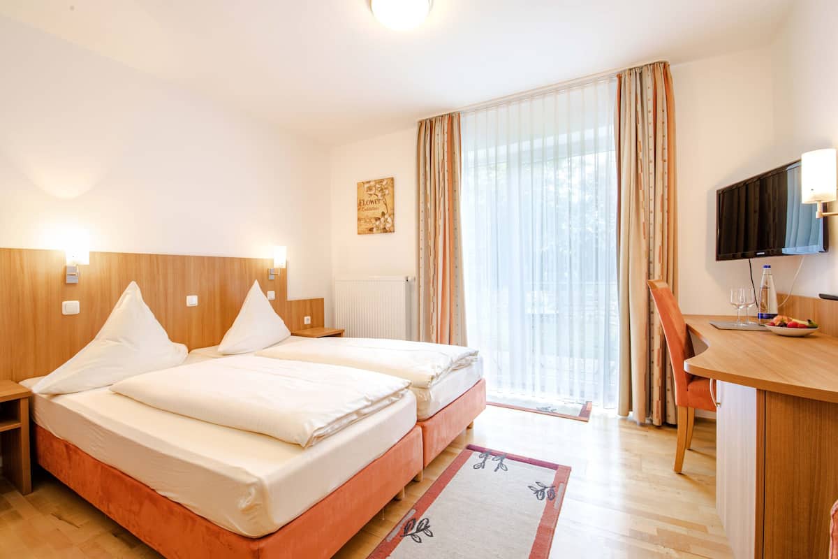 A hotel room with two beds, a desk, a chair, a television, and a window with curtains.