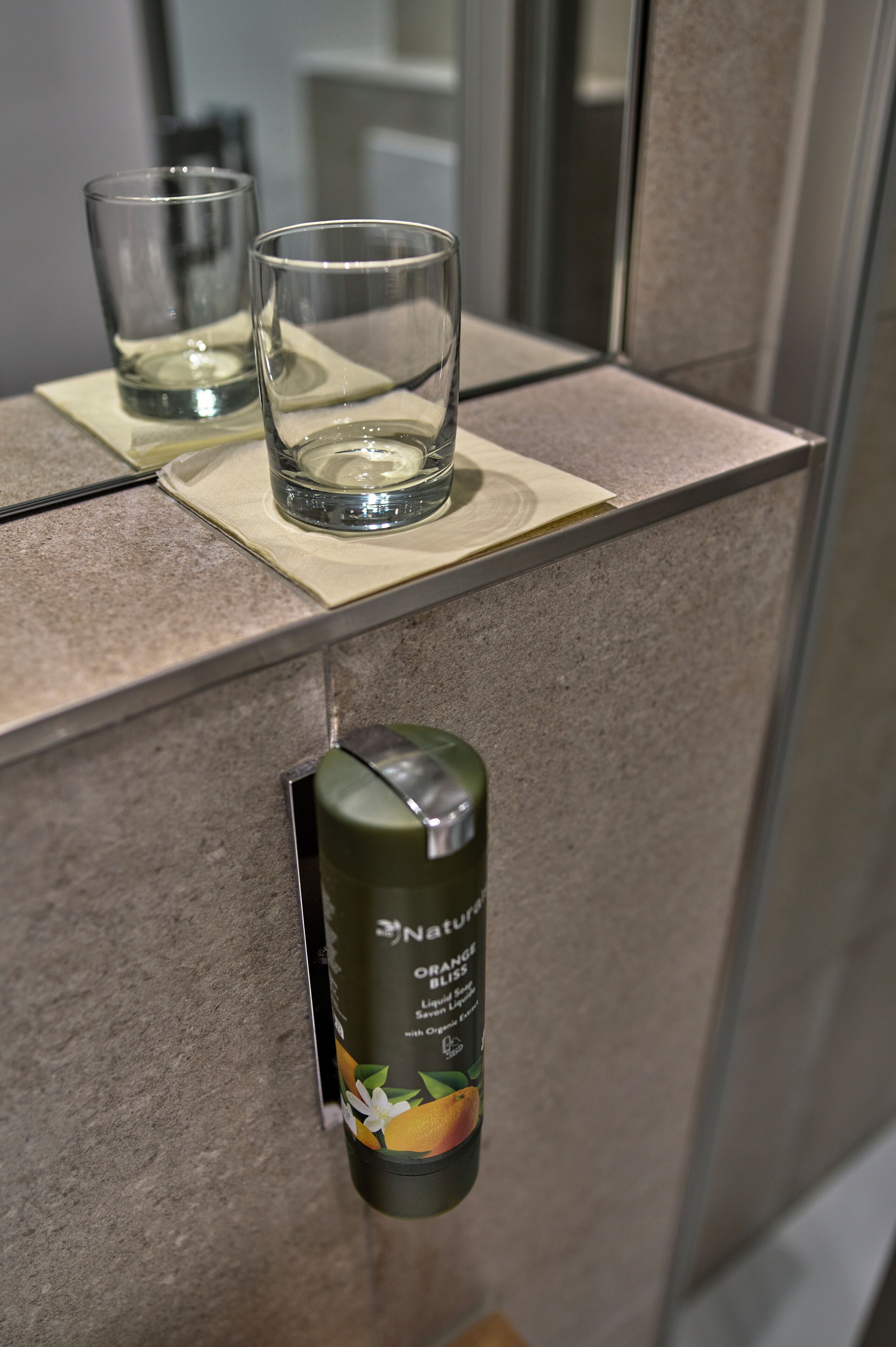 A bathroom counter with two glasses and a canister of organic liquid soap.