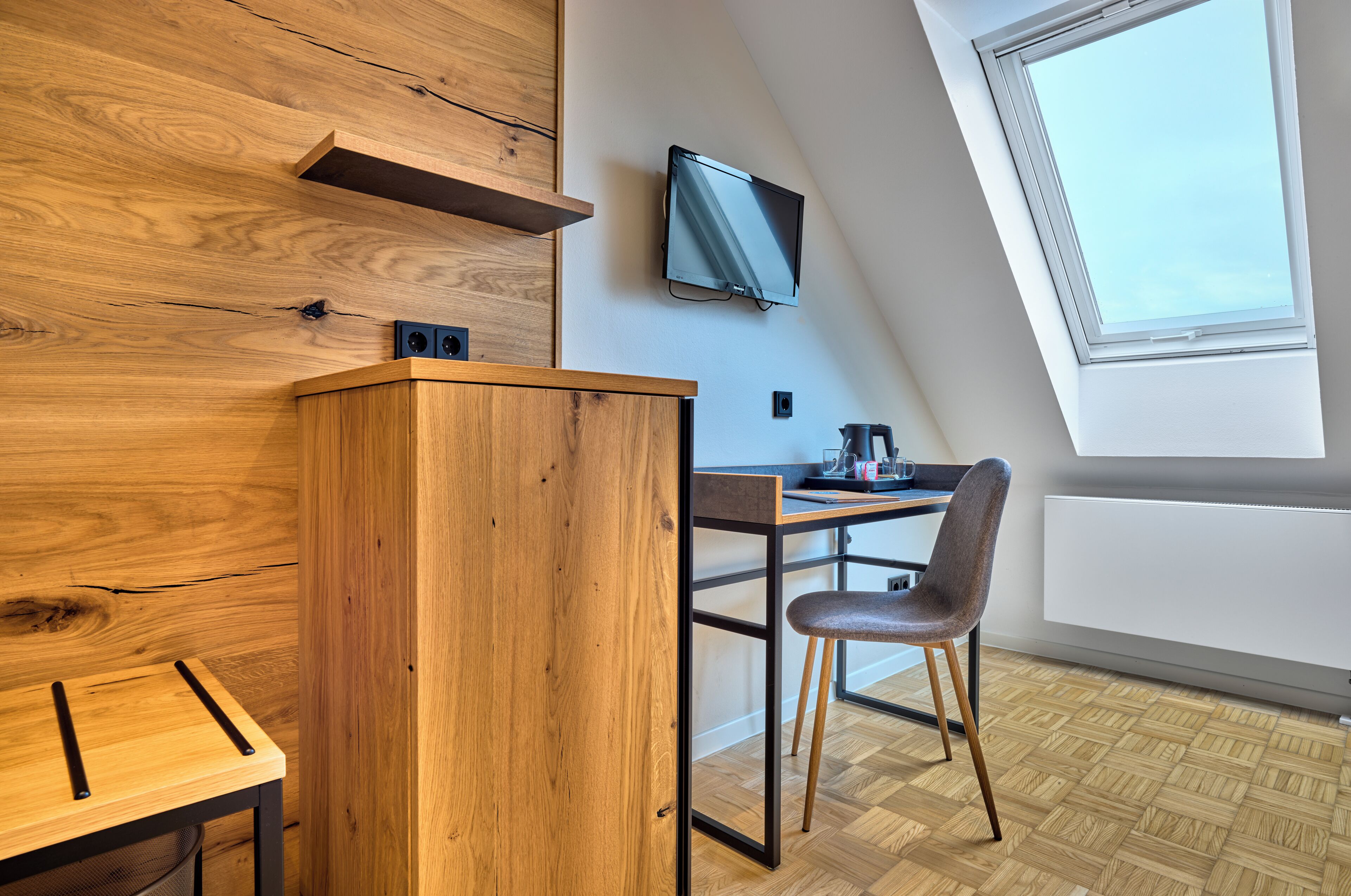 Una habitación moderna con una pared de acento de madera, un escritorio con silla, televisor montado y un ventanal grande.