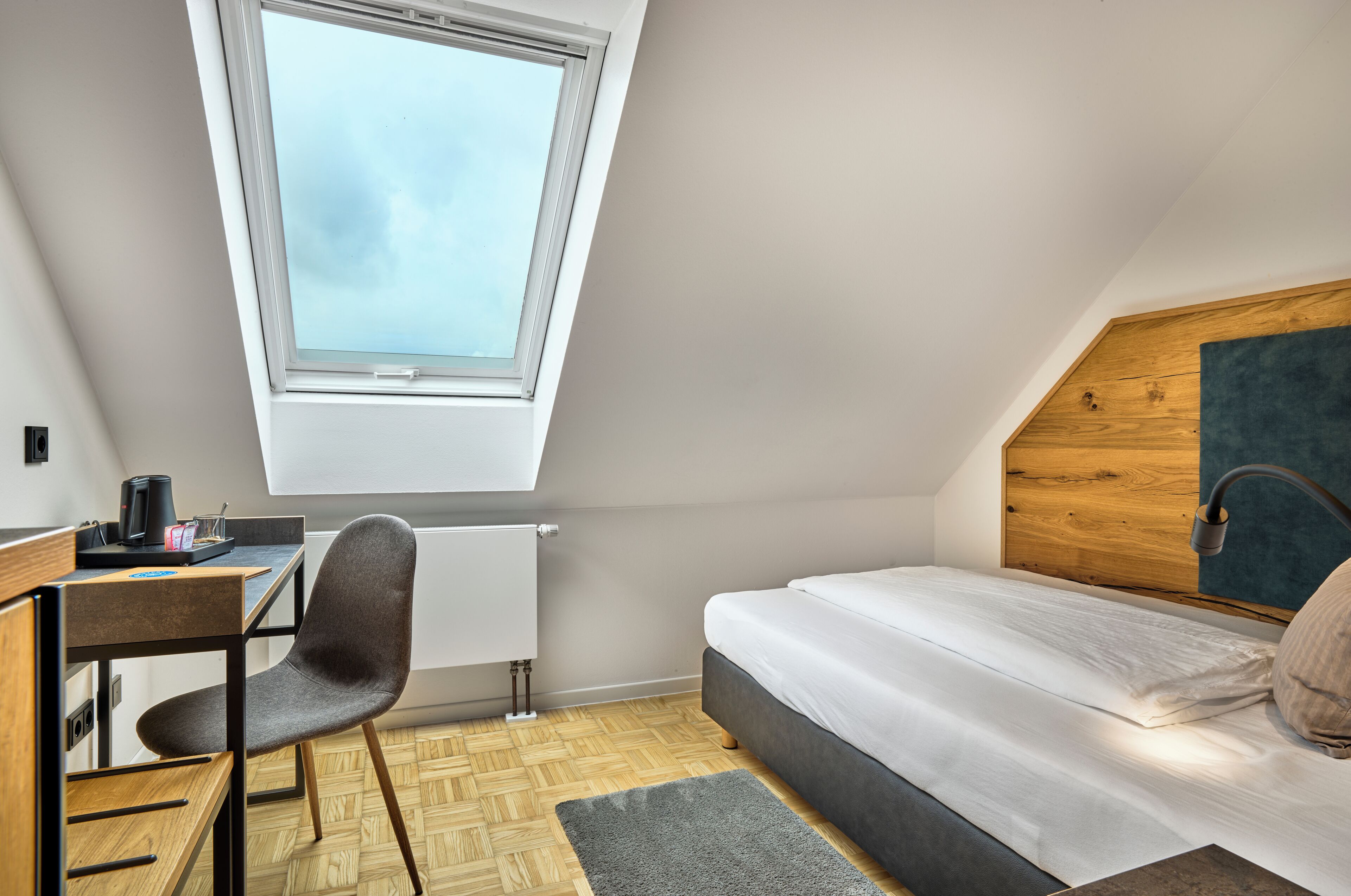 A compact room with a sloped ceiling, a bed, a desk, and a chair.