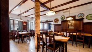 Un restaurante con mesas y sillas de madera, pilares de piedra y lámparas colgantes.