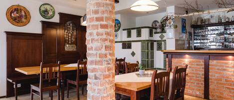 Un restaurante con mesas y sillas de madera, un pilar de ladrillo y una zona de bar con copas.