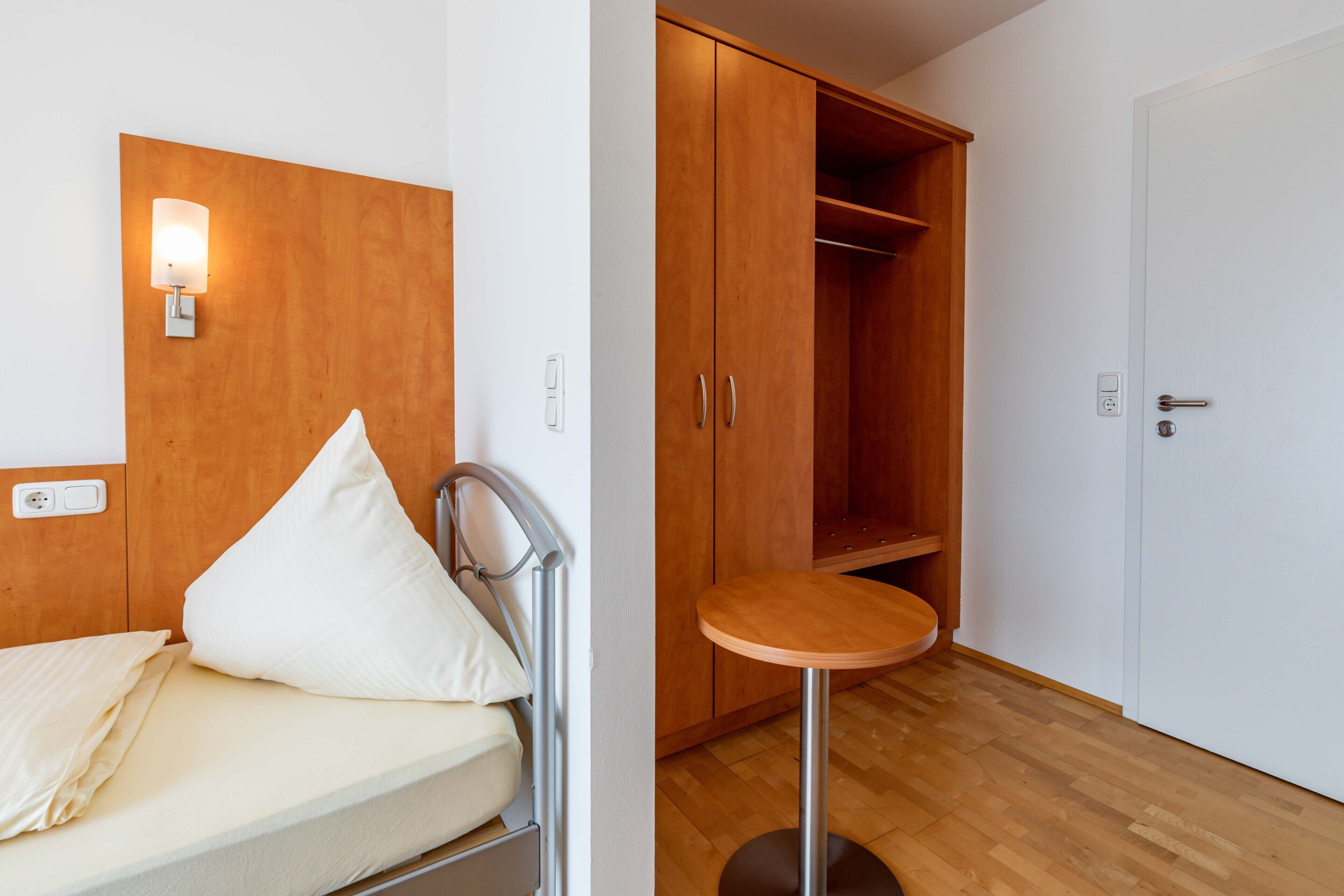 Quarto com cama, mesa de cabeceira, guarda-roupa e uma mesa redonda.
