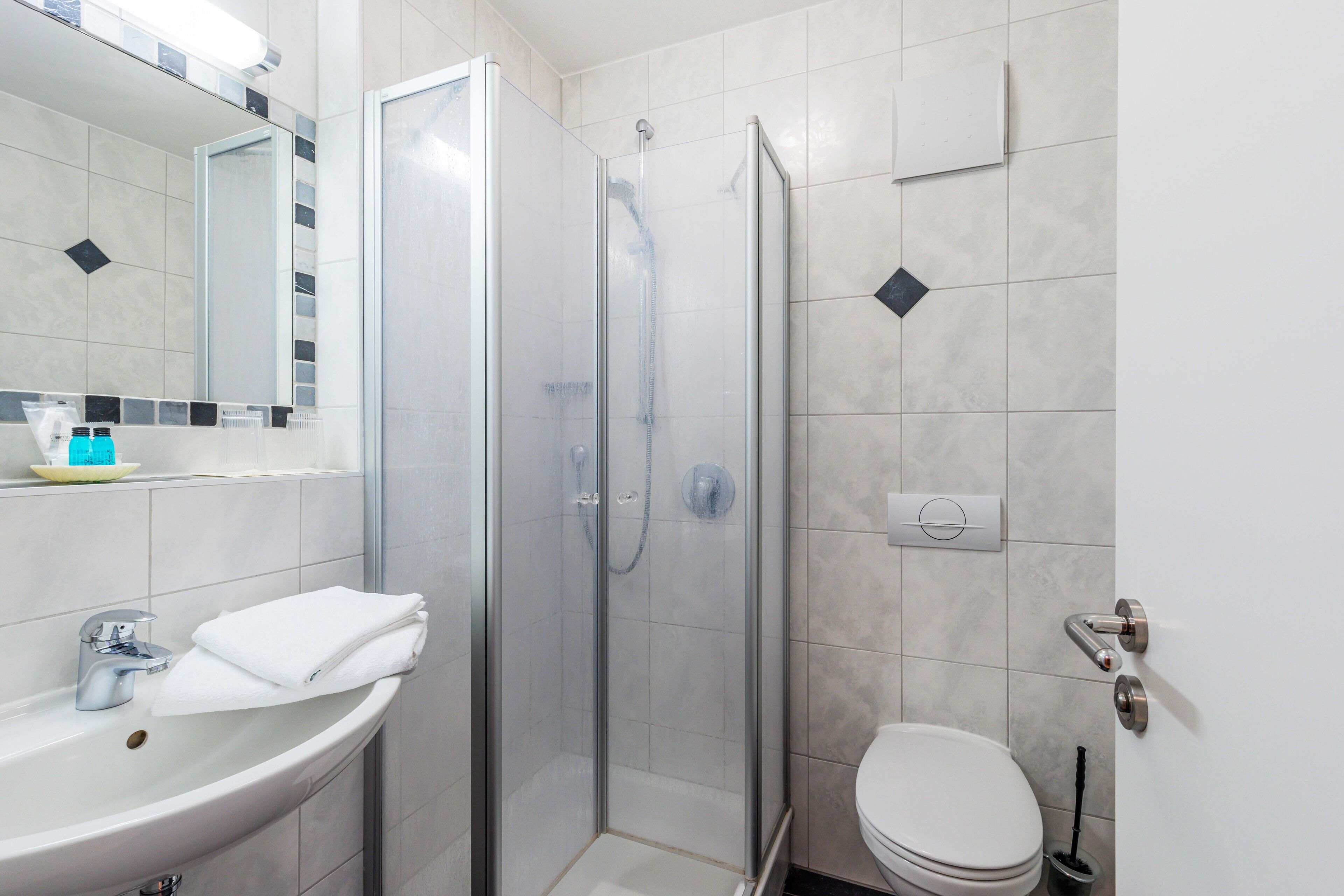 Un baño moderno con ducha de vidrio, lavamanos con toalla y retrete.