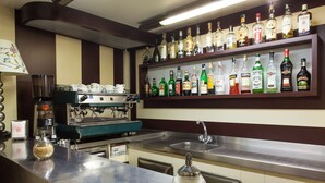 Zona de bar con una máquina de café, una variedad de botellas de licores en estanterías y una barra con un dispensador de azúcar.