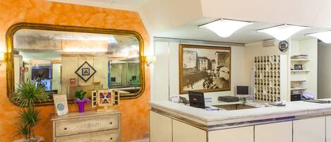 A reception area with a check-in counter, a large mirror, a potted plant, and a framed picture on the wall.