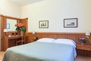 A hotel room with a bed, a desk, a chair, a mirror, and two framed pictures on the wall. - Hotel San Marco (Prato)