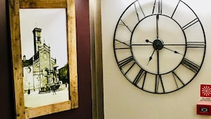 Un comedor con una mesa preparada para dos, un reloj de pared grande y un cuadro de un edificio.