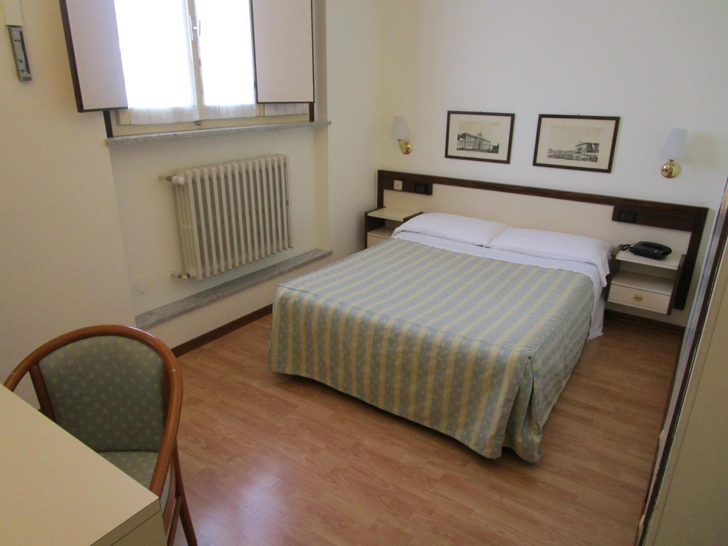 A hotel room with a bed, bedside table, lamp, and a chair.
