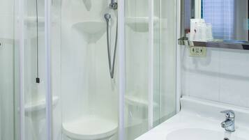 Un baño moderno con ducha de vidrio, lavamanos blanco y espejo sobre el lavamanos.