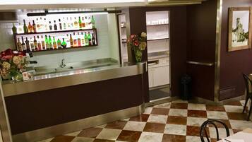 Un coin bar avec un sol à carreaux, un comptoir où sont exposées différentes bouteilles et un vase rempli de fleurs.