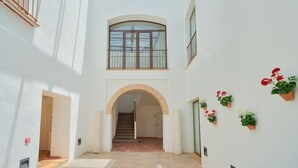 A spacious interior with a central staircase, white walls, and potted plants. - Tandem El Patio (Córdoba)