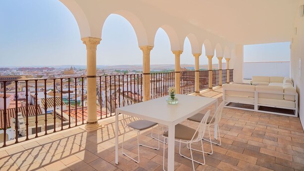 A balcony with a white table and chairs, a white sofa, and a view of a cityscape. - Tandem El Patio (Córdoba)