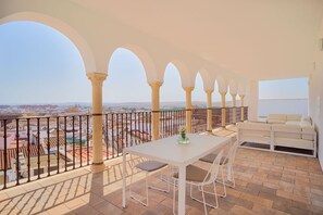 Un balcón con una mesa y sillas blancas, un sofá blanco y vistas de la ciudad.