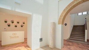A modern interior with a reception desk labeled 'Tandem Apartments', a stone column, and a staircase. - Tandem El Patio (Córdoba)