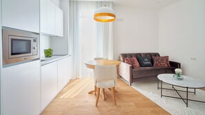 A compact living space with a kitchenette, a dining area, and a seating area with a sofa and a small round table. - Tandem El Patio (Córdoba)
