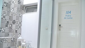 A bathroom with a tiled wall, a glass shower enclosure, and a door labeled '104 Pedra de Lume'. - Ouril Hotel Julia (Sal)