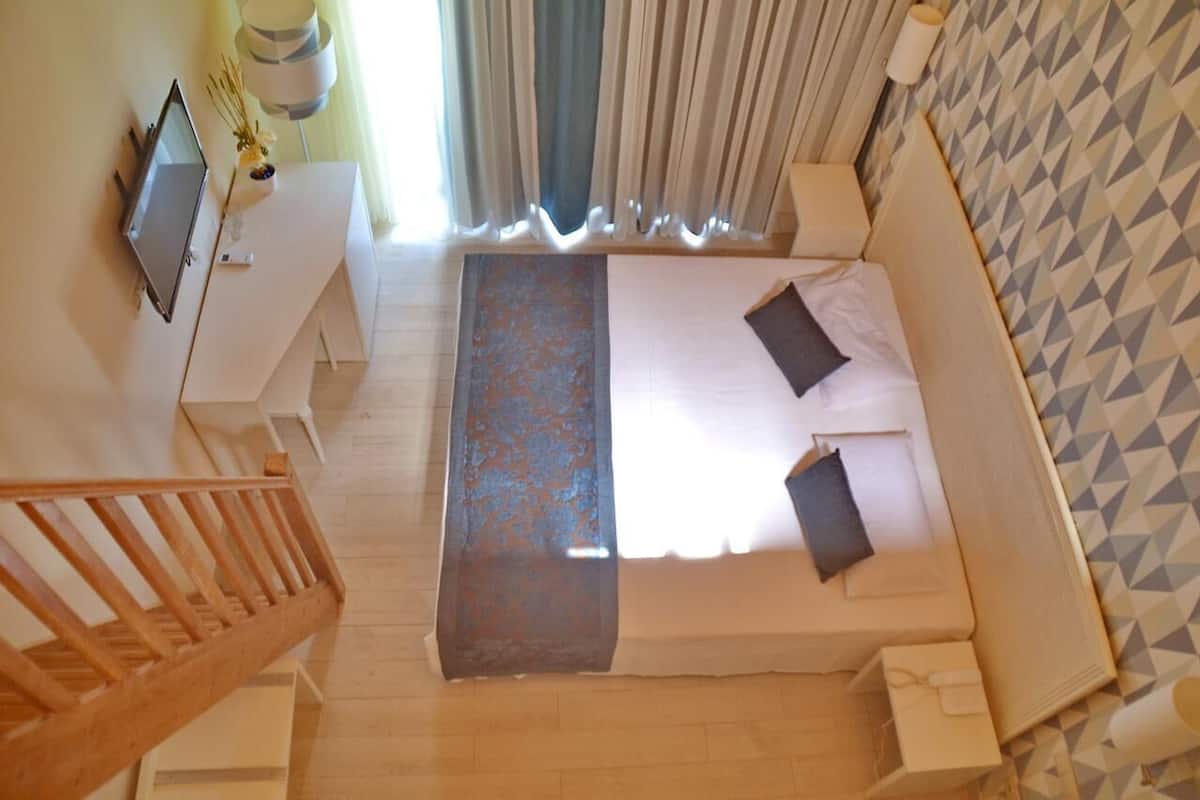 A bedroom with a bed, a desk, a TV, and a staircase.