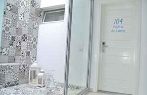 A bathroom with a tiled wall, a glass shower enclosure, and a door labeled '104 Pedra de Lume'. - Ouril Hotel Julia (Sal)