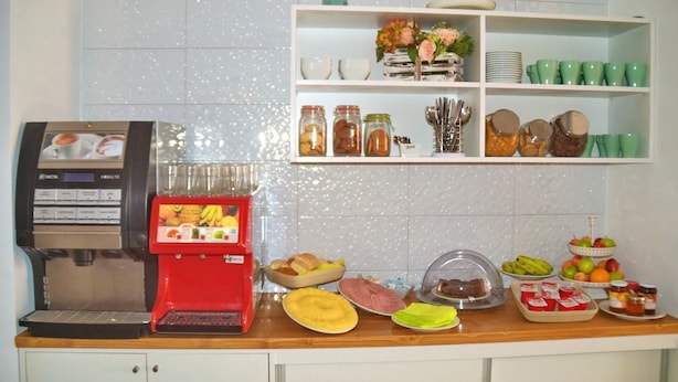 A breakfast buffet setup with a coffee machine, various food items, and a beverage dispenser. - Ouril Hotel Julia (Sal)