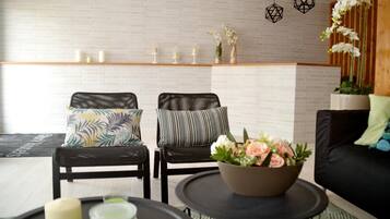 A modern living room with two black chairs, a black sofa, a round coffee table with a floral centerpiece, and a brick-patterned wall.